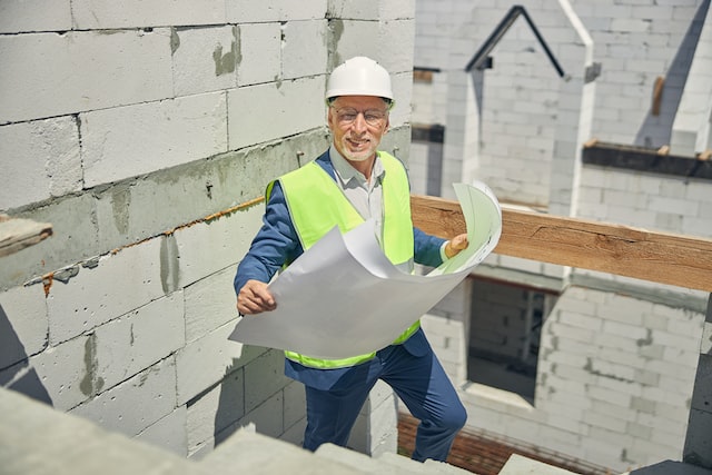 joyous senior male engineer in a safety vest holding house plans